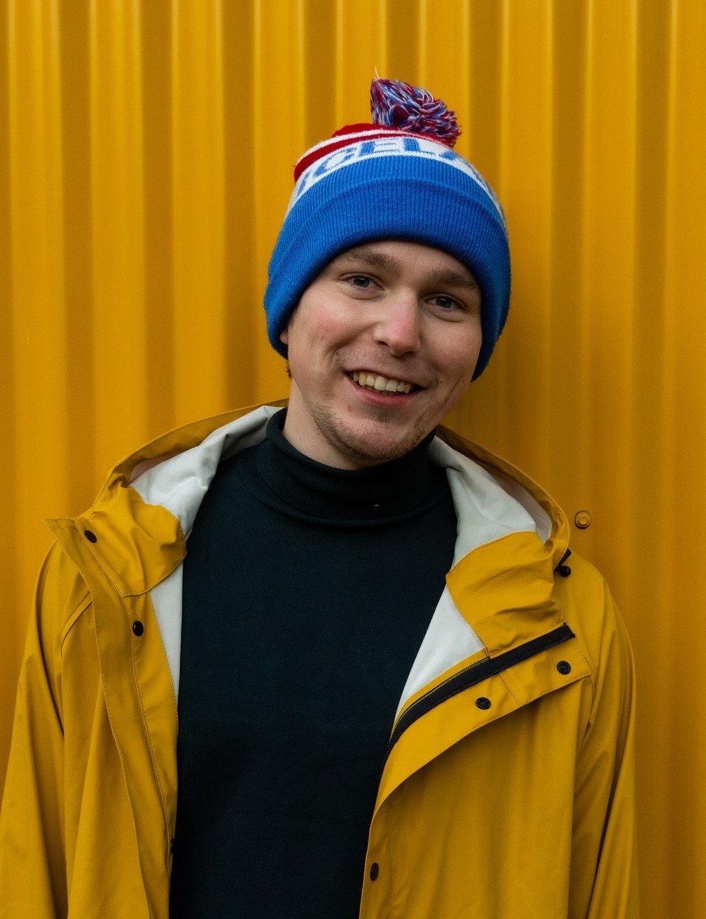 Portret Jędrzeja na żółtym tle, w niebieskiej ciepłej czapce i żółtej kurtce.