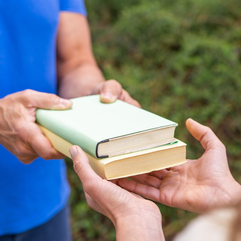 ludzie podają sobie książki z rąk do rąk.