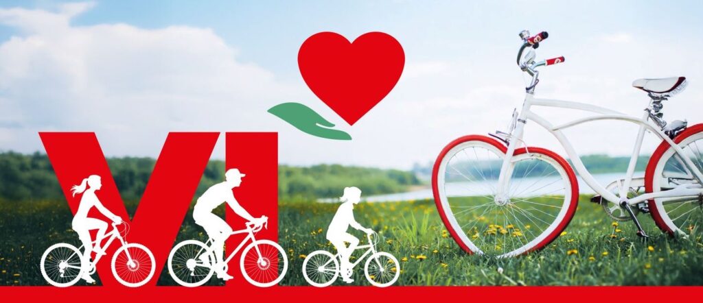 Plakat promujący rajd rowerowy dla hospicjum w Wałbrzychu. Na tle zielonej łąki widać biały rower z czerwonymi oponami oraz sylwetki trzech osób jadących na rowerach. Nad nimi znajduje się czerwone serce trzymane przez zieloną dłoń. Na dole widoczny napis: »VI Rajd Rowerowy dla Hospicjum w Wałbrzychu«.