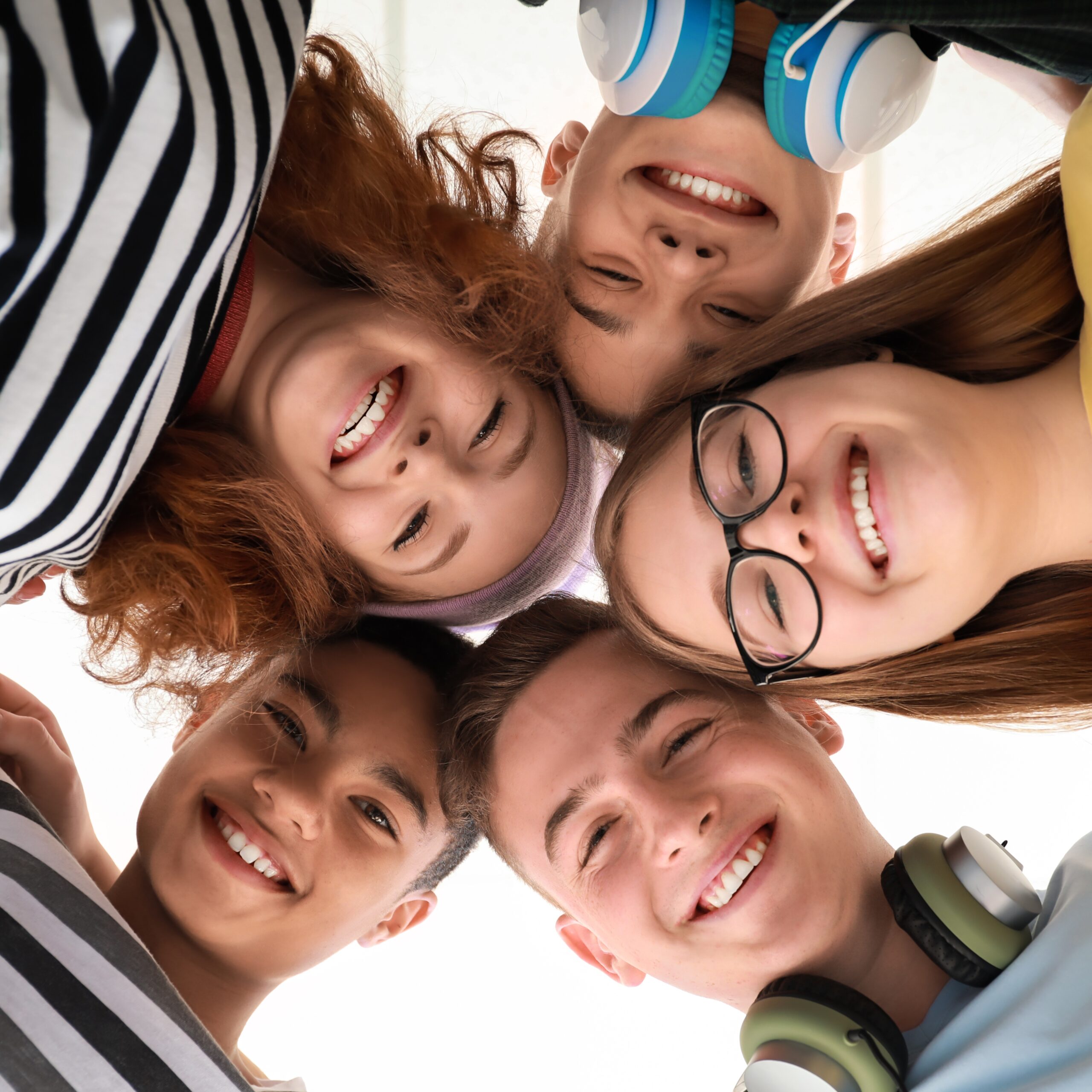 pięcioro nastolatków, uśmiechają się i stykają głowami, osoba robiąca zdjęcie znajduje się poniżej ich głów.