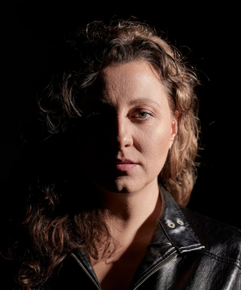 Nadia Szagdaj, portret, pół twarzy w cieniu, skórzana czarna kurtka, kobieta w średnim wieku, lekko kręcone włosy