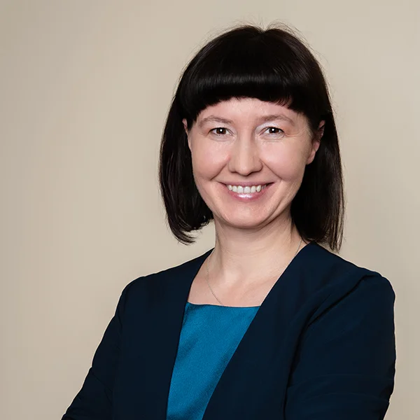 Joanna Przybylowska, kobieta ma krótkie czarne włosy, obcięte geometrycznie włosy, w tle beżowe tło. Kobieta się uśmiecha.