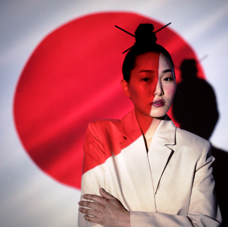 japonka w tradycyjnej fryzurze, beżowej garsonce, odbija się na niej i na tle czerowona duża kropka - nawiązanie do flagi Japonii.