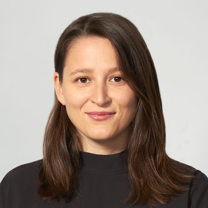 Osoba o średniej długości brązowych włosach, ubrana w ciemną bluzkę, sfotografowana na jasnym, neutralnym tle.