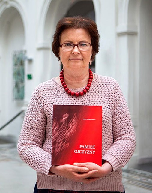 Beata Stragierowicz  w różowej bluzce i koralach pozuje ze swoją książką Pamięć Ojczyzny.