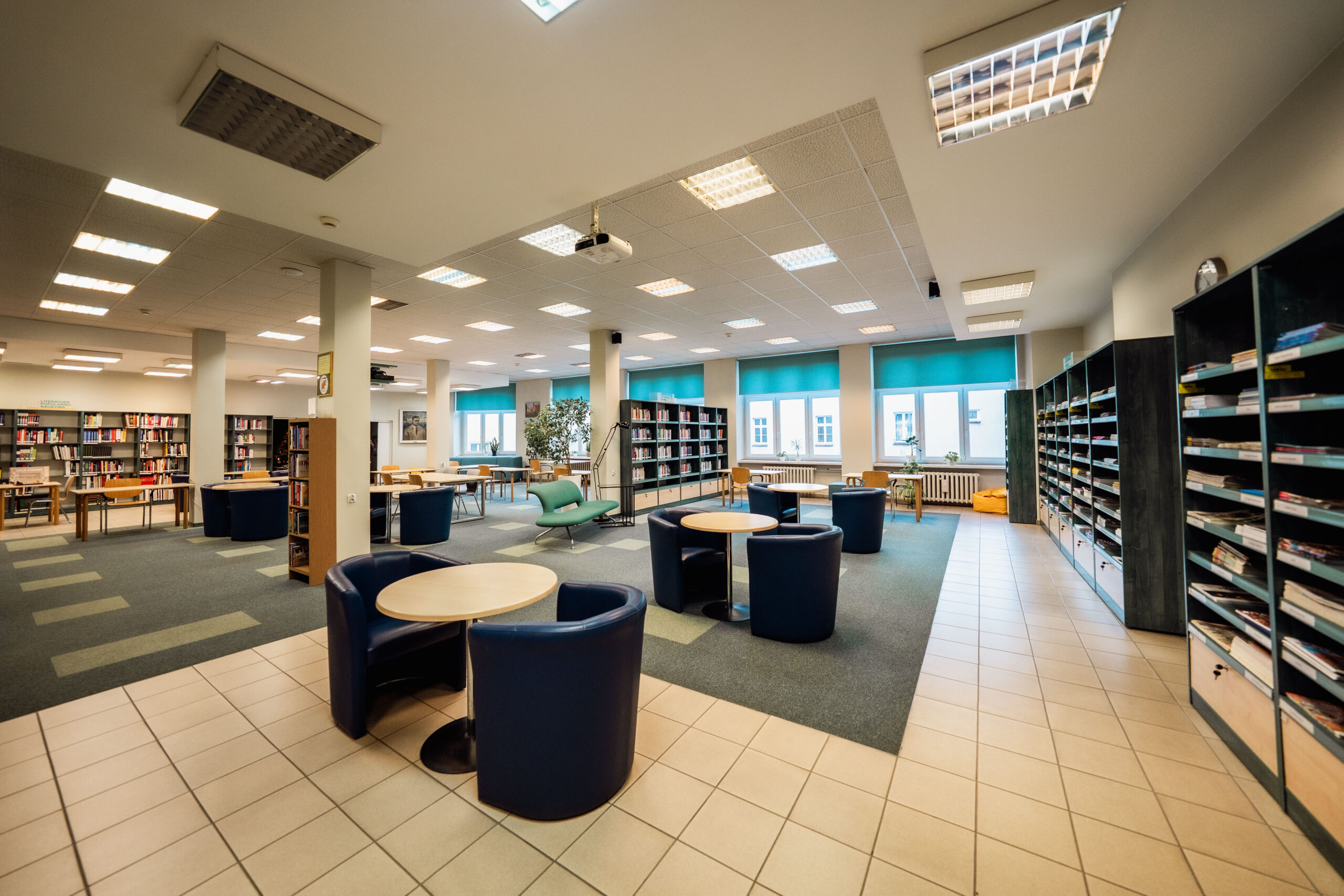 wnętrze biblioteki zasobów popularnonaukowych, stoliki, fotele, duże okna i regały z książkami