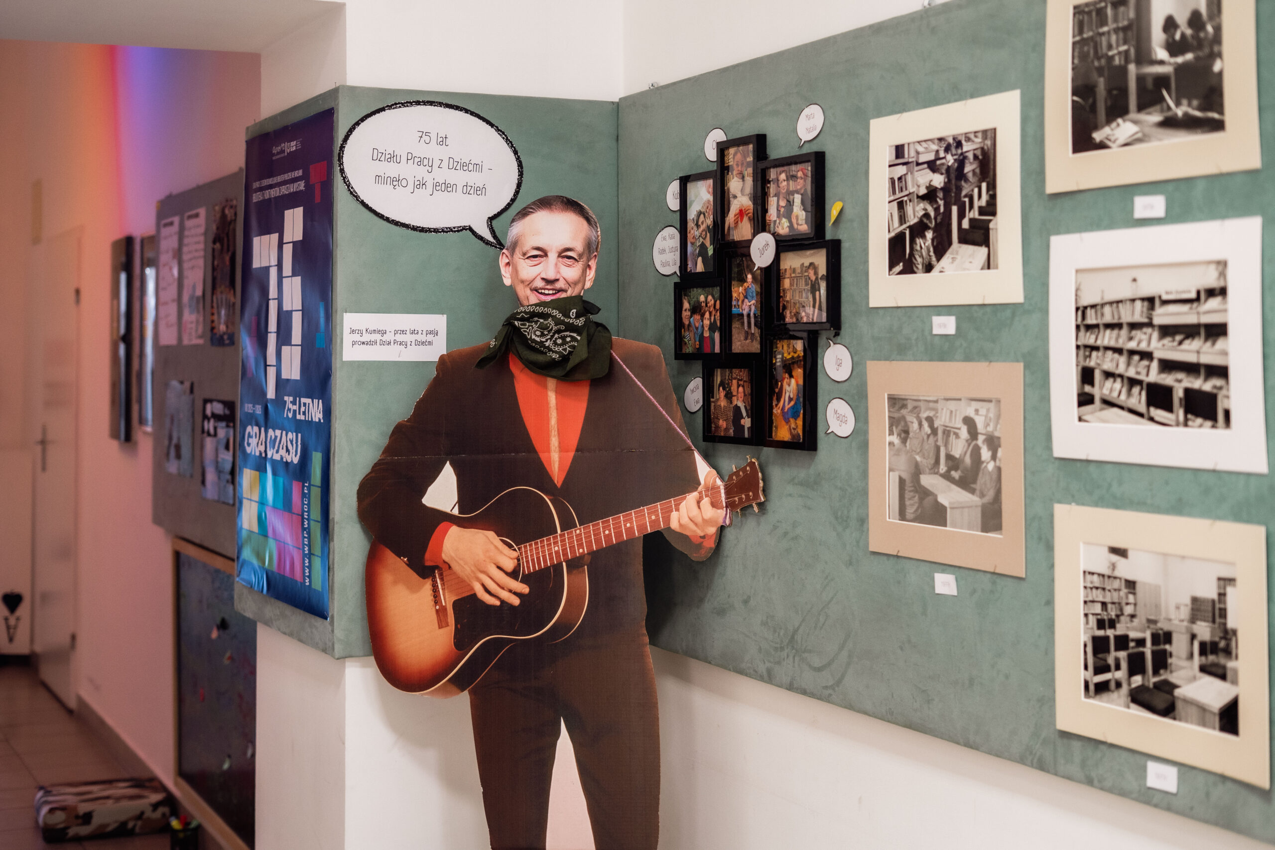 korytarz, na ścianie wysatwa zdjęć i chmurki komiksowe, na środku stoi papierowa postać z gitarą