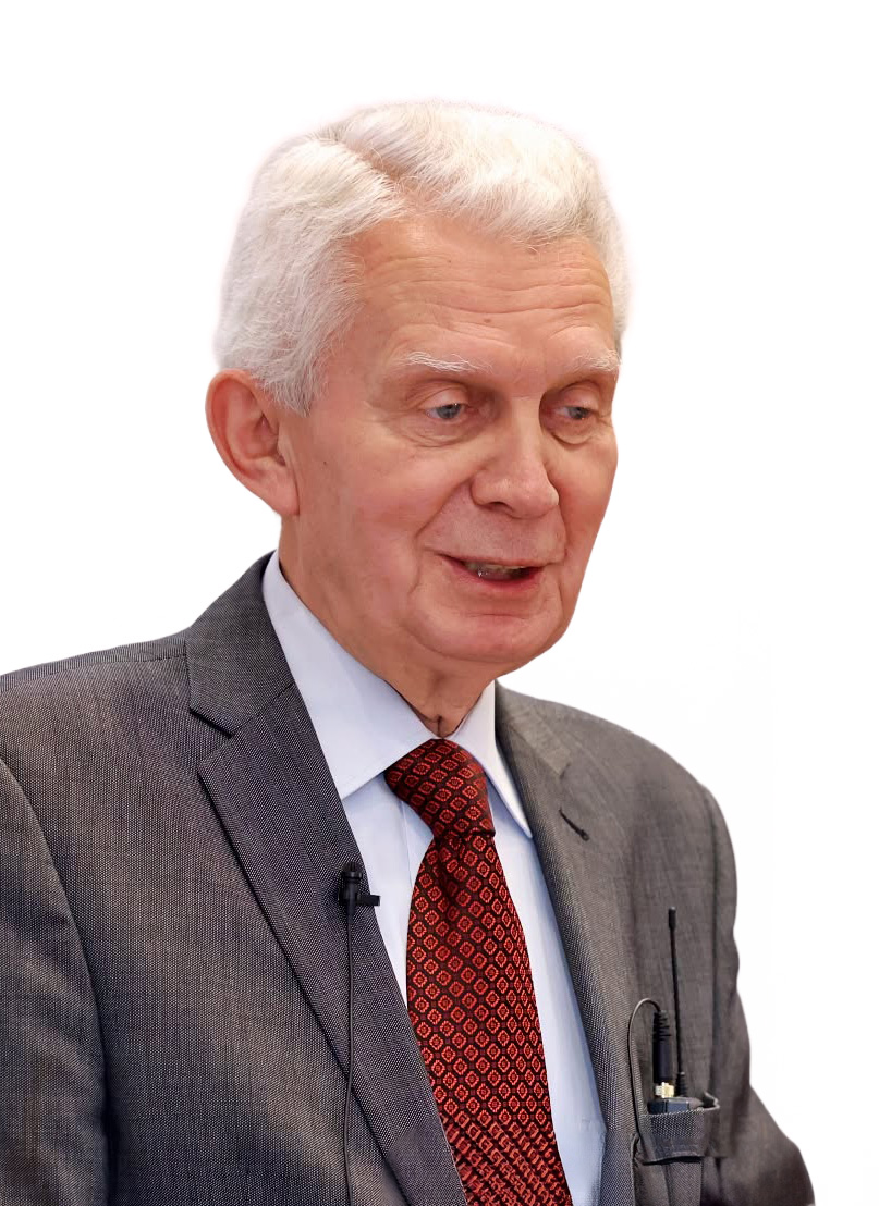 starszy mężczyzna w garniturze, ma czerwony krawat, podpięty mały mikrofon, jest siwy i mówi, tło białe