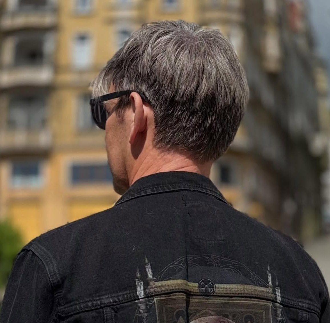 siwy mężczyzna tyłem stoi w dzinsowej kurtce