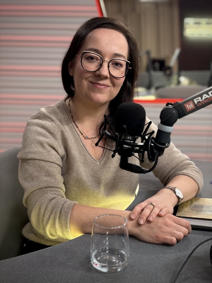 kobieta, ciemne włosy, okulary, siedzi przed mikrofonem radiowym