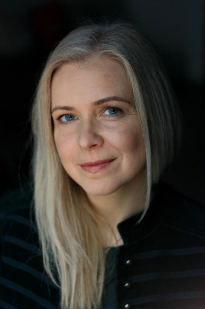 kobieta, lekko się uśmiecha, blond włosy długie, ciemne tło, portret
